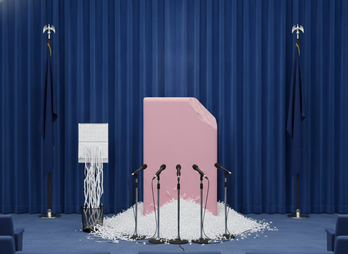 Press photo: a press-briefing lectern replaced by a giant pink pencil eraser, rubber shavings piled on the floor like snow beside a shredded wall calendar, plain flags either side